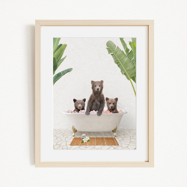 A framed image depicting three bears sitting in a bathtub filled with flowers, surrounded by tropical plants.