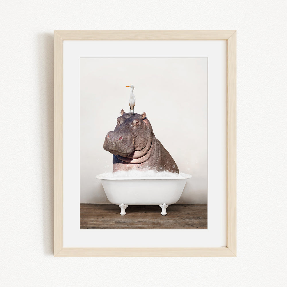 A framed image depicting a large hippopotamus sitting in a bathtub, with a seagull perched on its head.