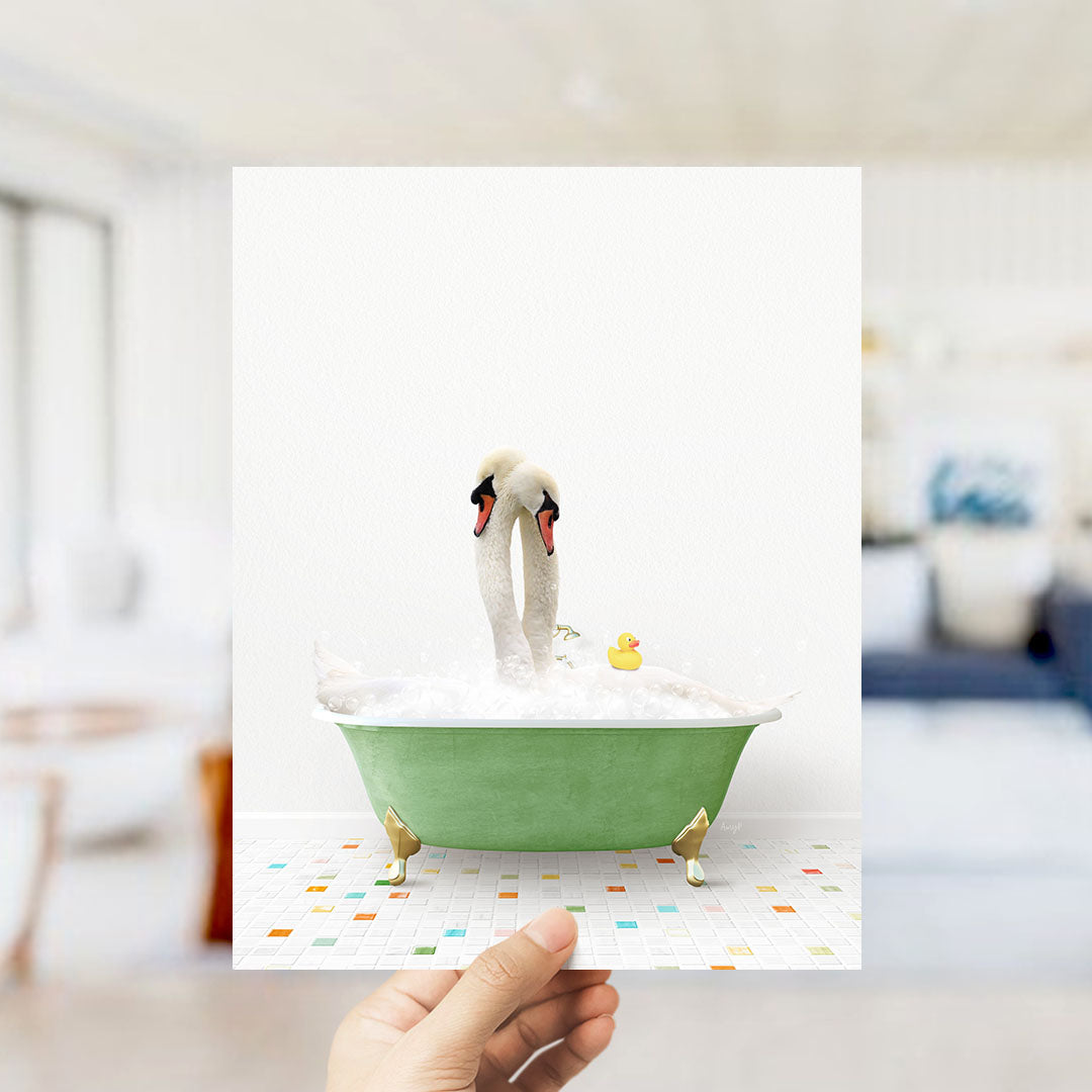 A hand holds up a framed image depicting a white swan standing in a green bathtub filled with bubbles, with a yellow rubber duck floating nearby.