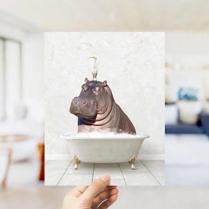 A hand holds up a framed image of a hippopotamus sitting in a bathtub, with a seagull perched on its head.