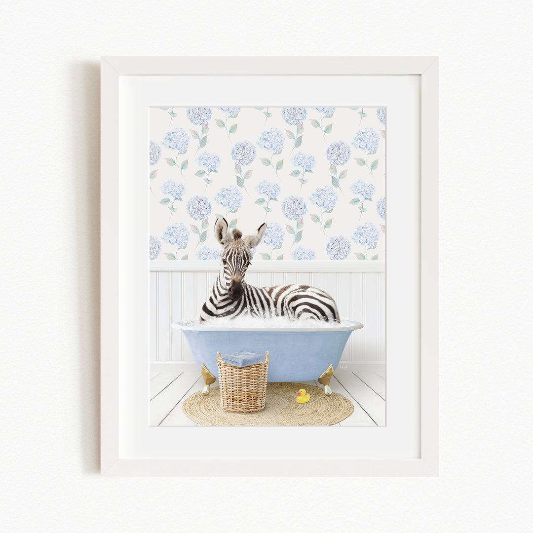 A zebra is sitting in a blue bathtub filled with water, surrounded by a wicker basket and yellow rubber ducks.