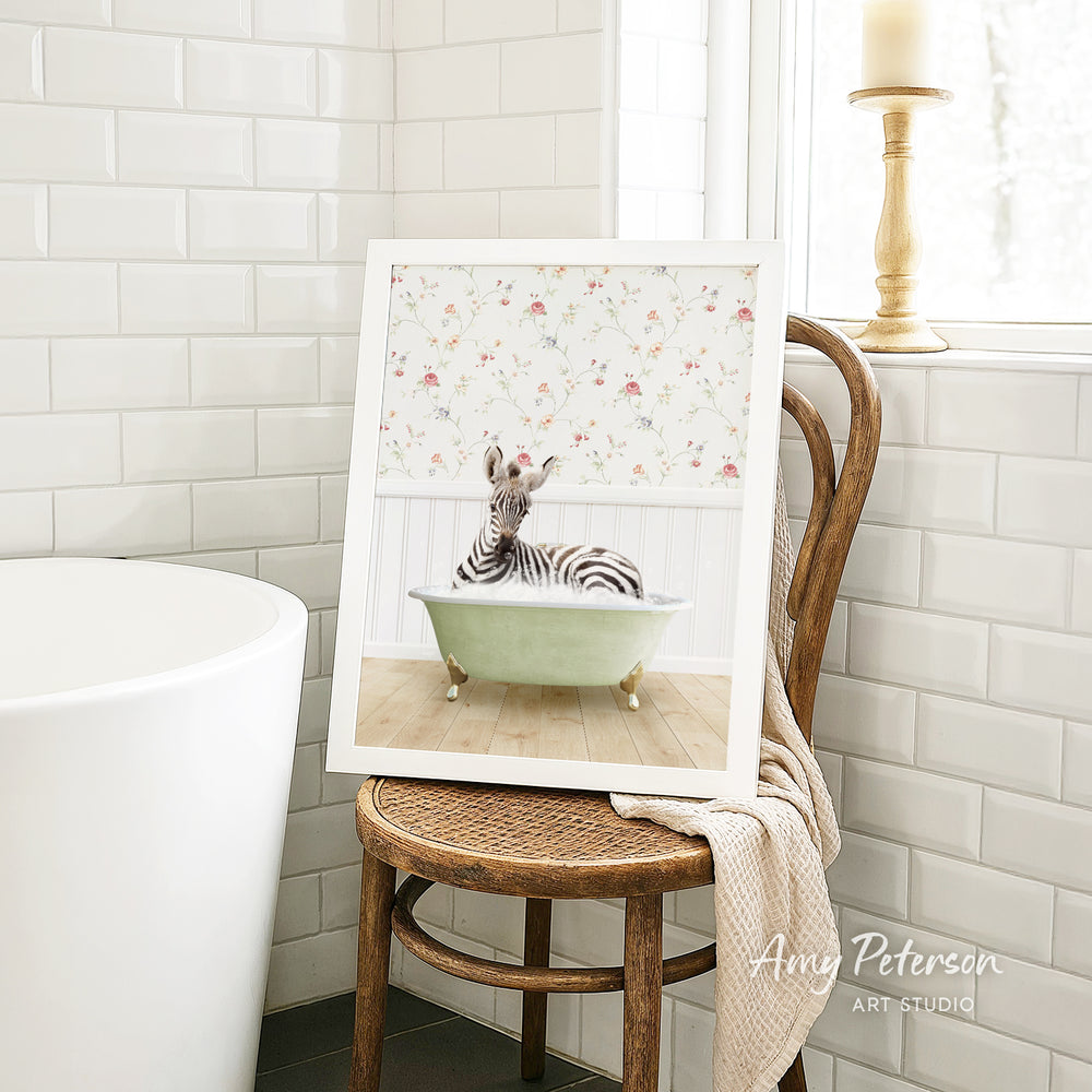 A framed image of a zebra sitting in a bathtub is displayed on a wooden chair in a bathroom setting.