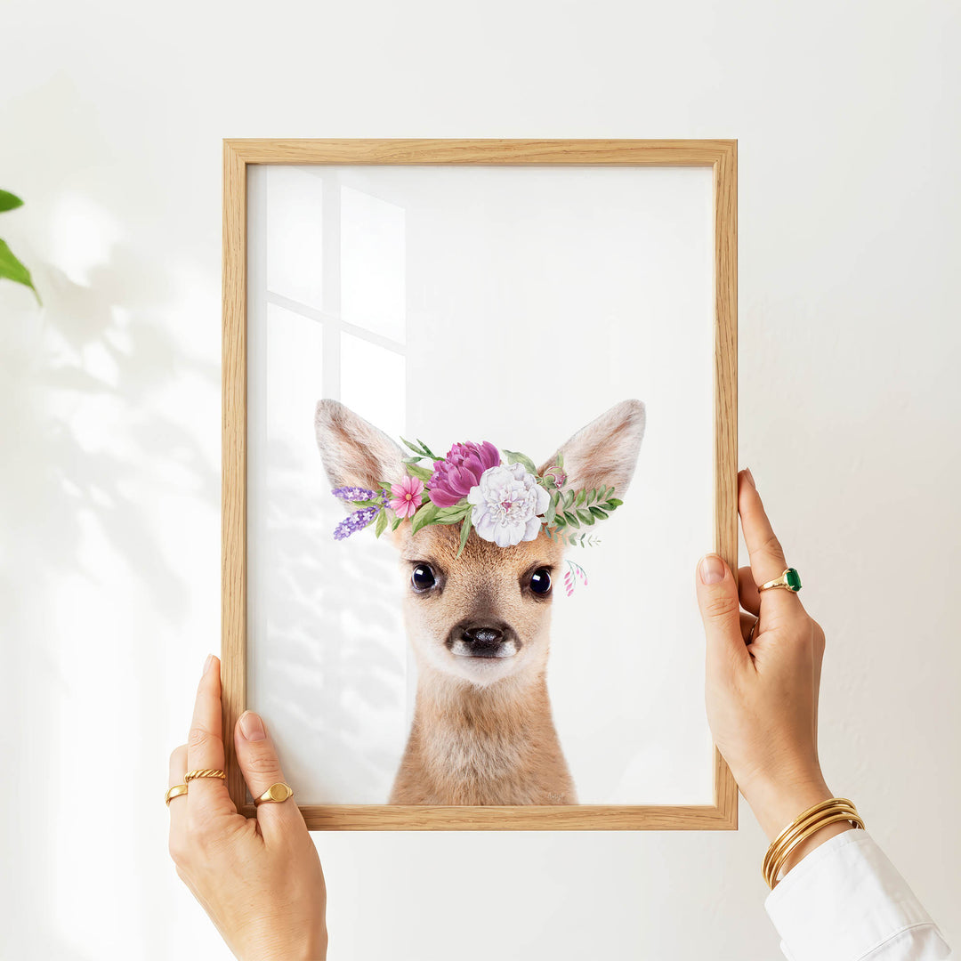 A person's hands are holding a wooden frame with a picture of a deer wearing a flower crown.
