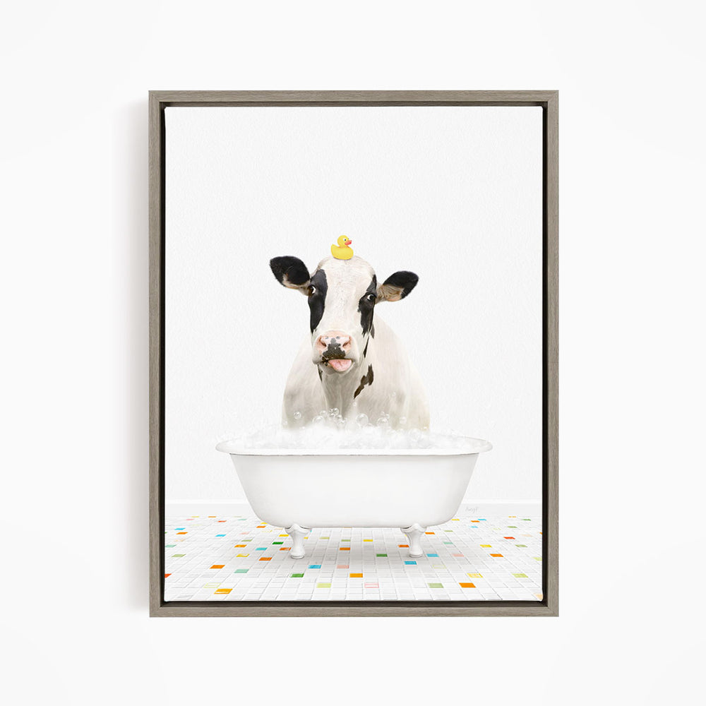 A black and white cow is sitting in a white bathtub filled with bubbles, with a rubber duck perched on its head.