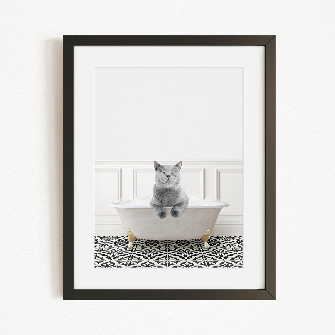 A gray cat sitting in a white bathtub with gold legs, surrounded by a black and white patterned rug on the floor.