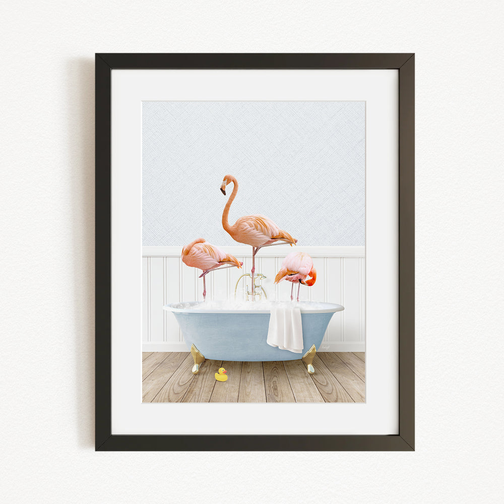 A framed image depicting three flamingos standing on a blue bathtub, with a towel draped over the side of the tub.