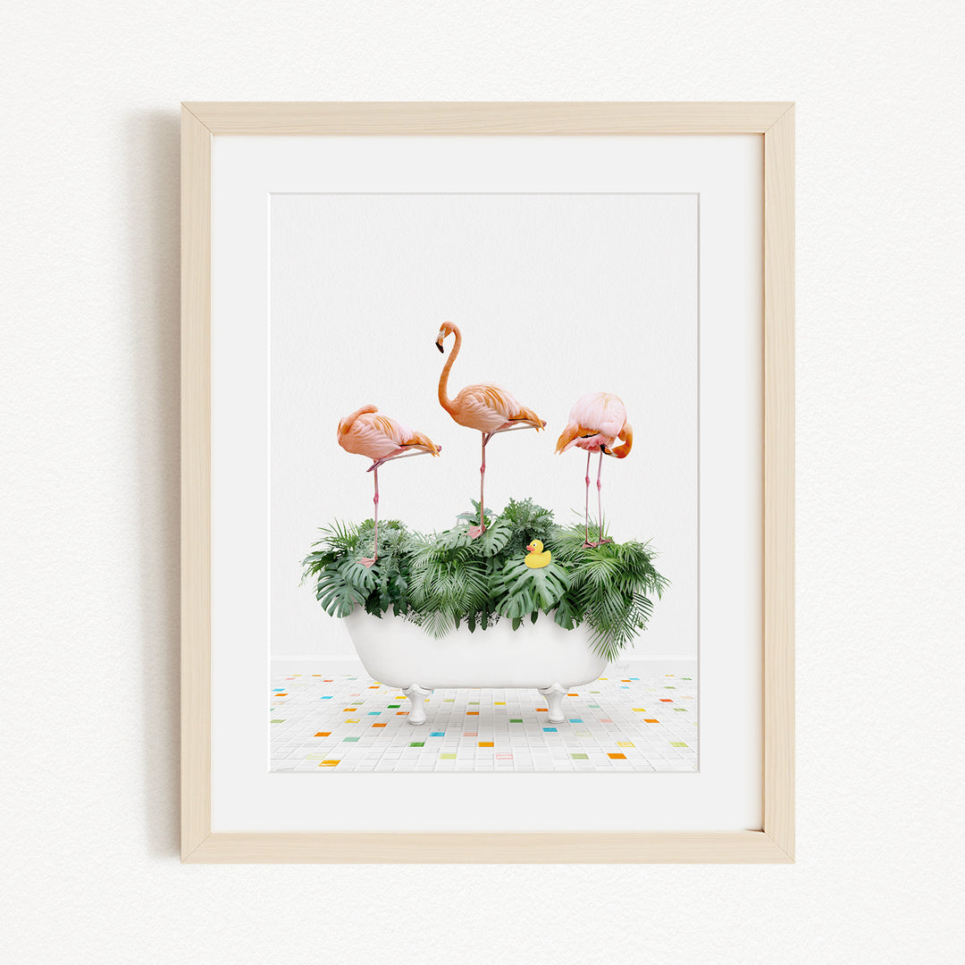 A framed image depicting three flamingos standing on a white bathtub filled with green plants and flowers, set against a white background.