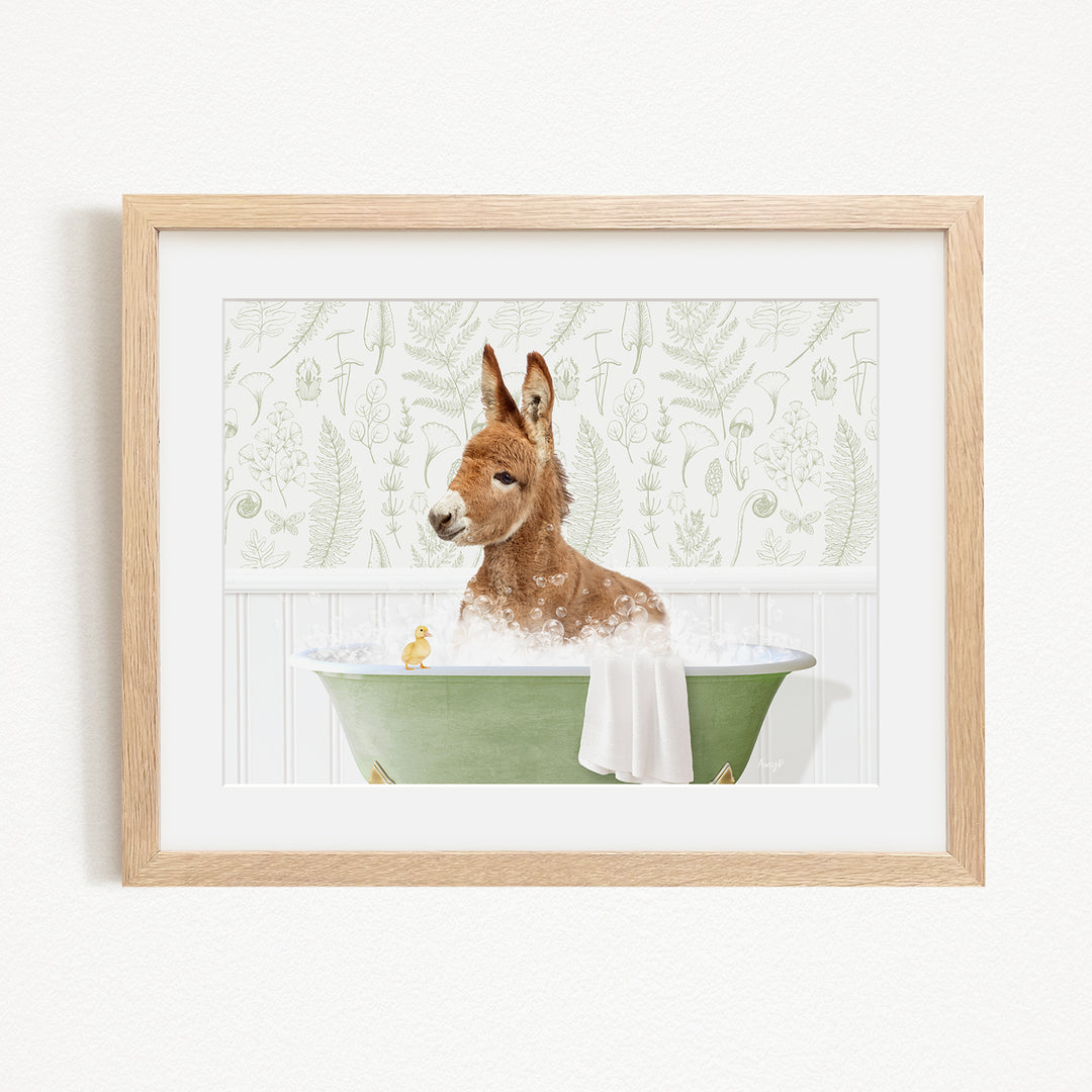 A brown alpaca is sitting in a green bathtub filled with water, surrounded by a white wall with a green plant pattern.