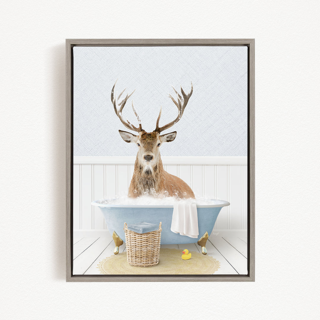 A deer with antlers is sitting in a bathtub filled with water, surrounded by a basket, a rubber duck, and a towel.