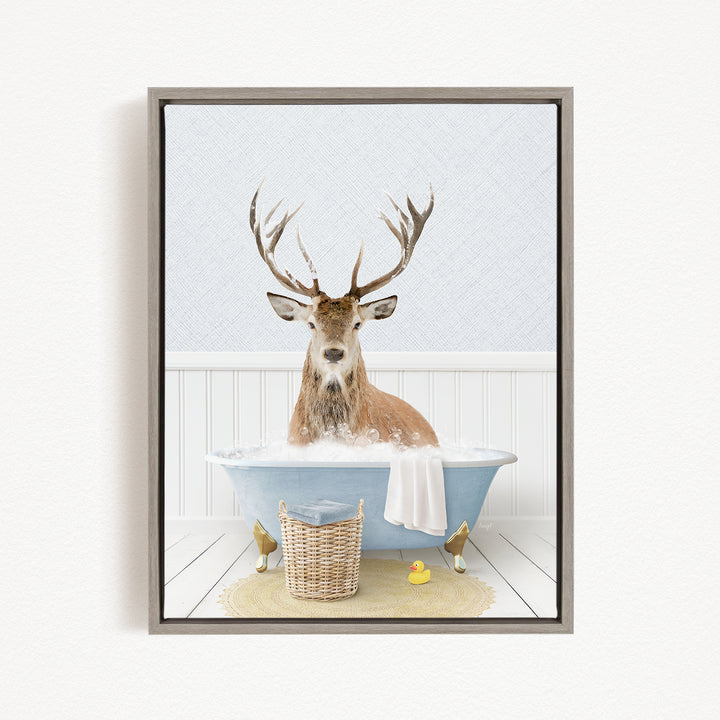 A deer with antlers is sitting in a bathtub filled with water, surrounded by a basket, a rubber duck, and a towel.