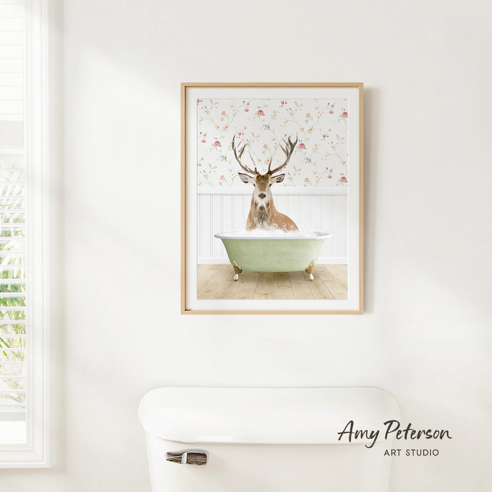 A framed image of a deer sitting in a bathtub, with a floral pattern on the wall behind it.