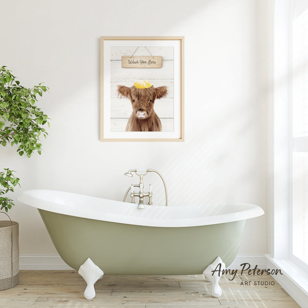 a green clawfoot bathtub with a framed picture of a cow above it, set against a white wall with a window.