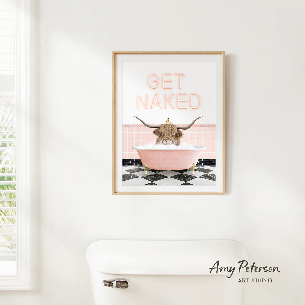 A framed poster with a cartoon image of a horned animal, likely a yak, sitting in a pink bathtub with the text "GET NAKED" on it.