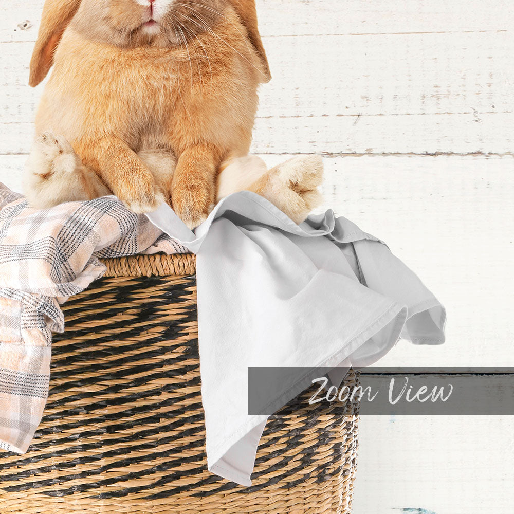 A small orange rabbit sitting in a woven basket, with a white cloth or blanket on top.