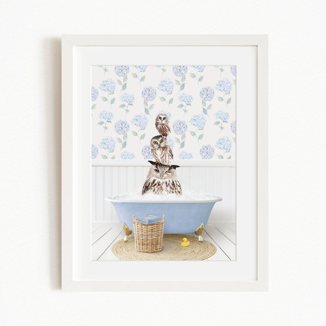 A framed image depicting a brown owl sitting in a blue bathtub filled with water, surrounded by a white floral pattern on the wall.