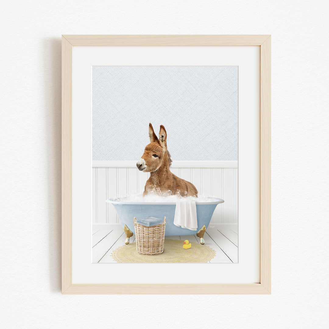 A donkey is sitting in a blue bathtub filled with bubbles, surrounded by rubber ducks and a yellow towel.