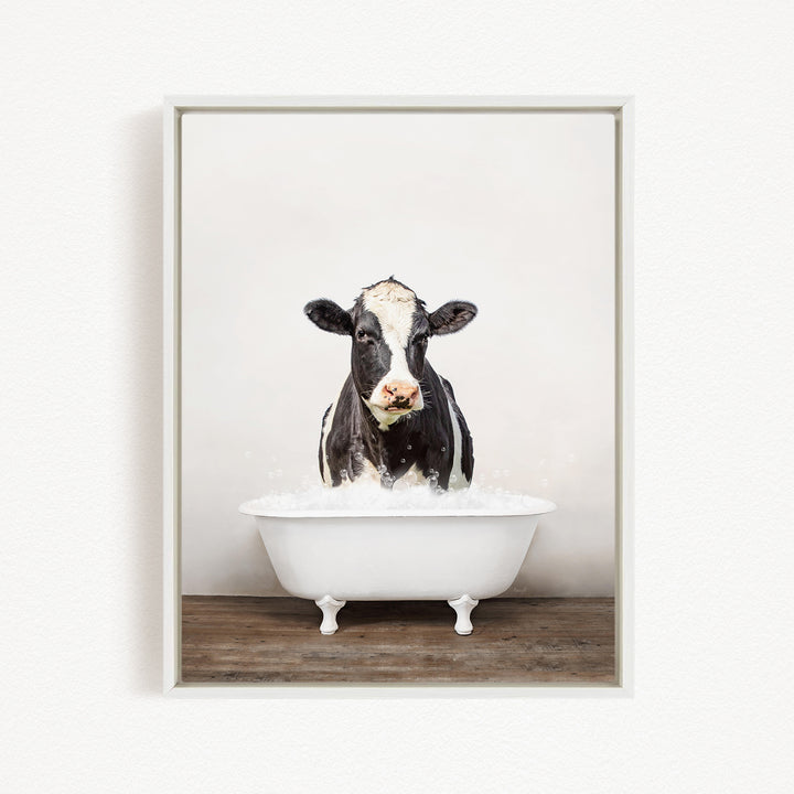 A black and white cow standing in a white bathtub filled with water, creating a whimsical and humorous scene.