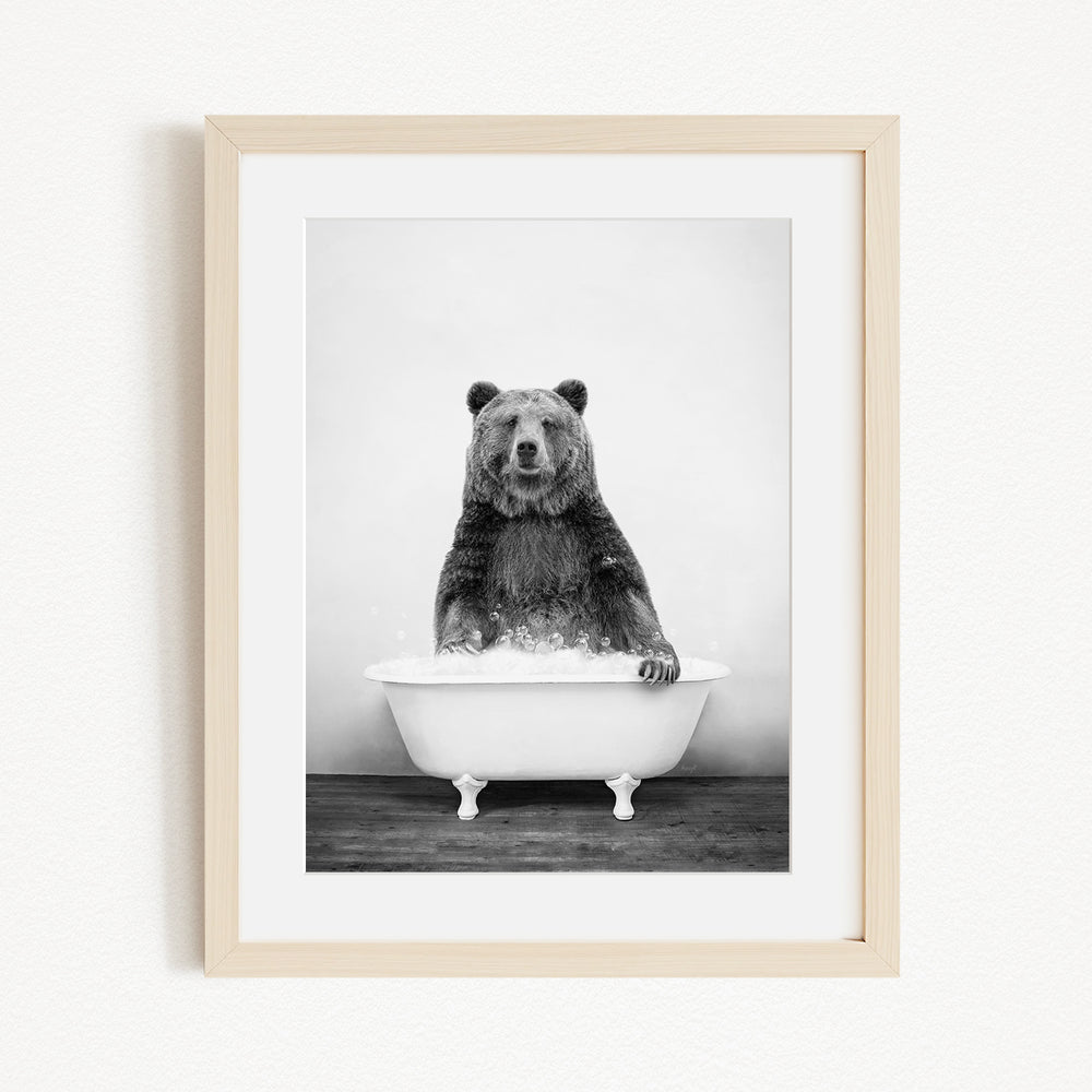 A black and white photograph of a bear sitting in a bathtub filled with water.