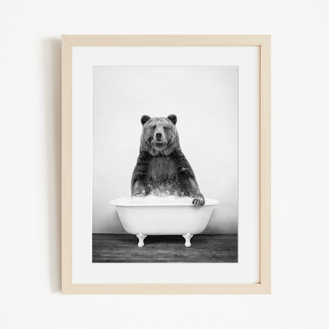 A black and white photograph of a bear sitting in a bathtub filled with water.