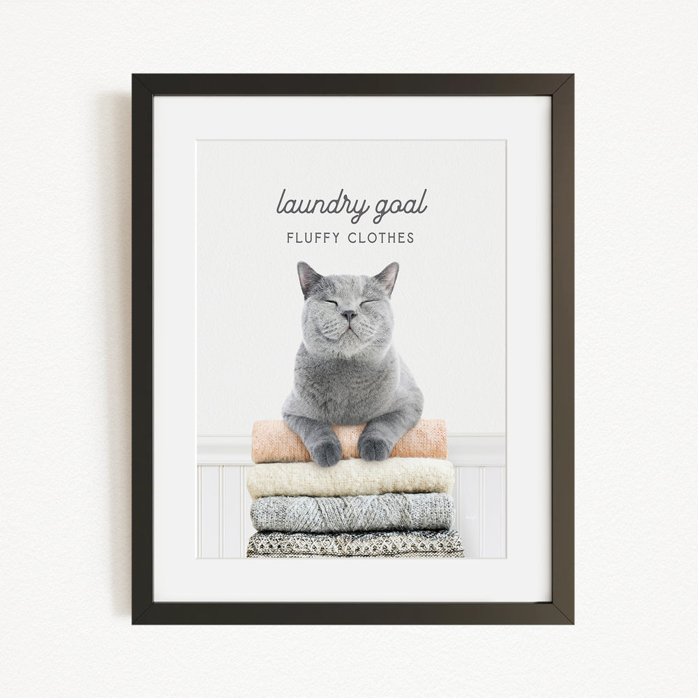 A framed image of a gray cat sitting on a stack of folded clothes, with the text "laundry goal" and "fluffy clothes" written above it.