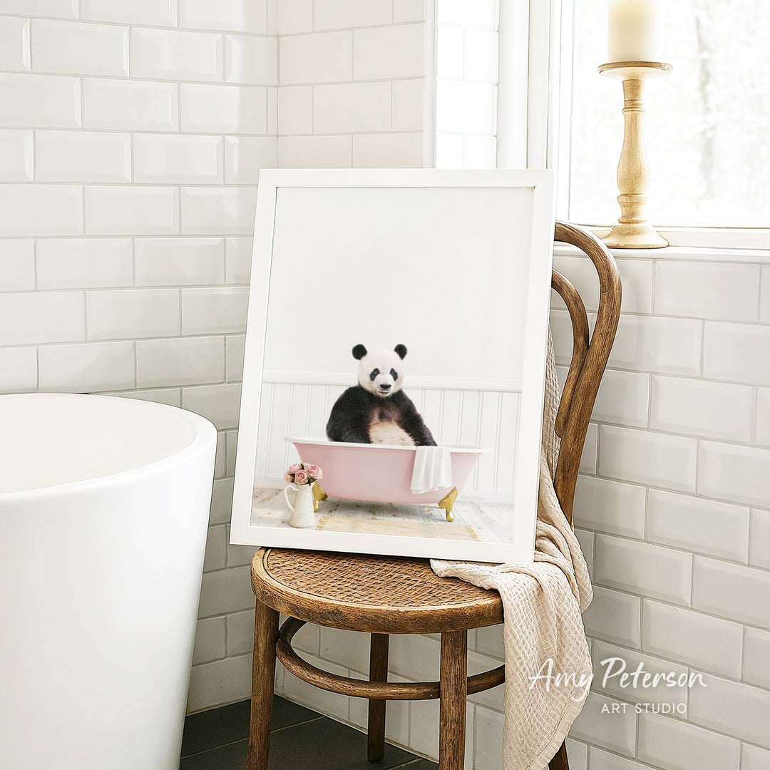A framed image of a panda sitting in a pink bathtub is displayed on a wooden chair in a bathroom setting.