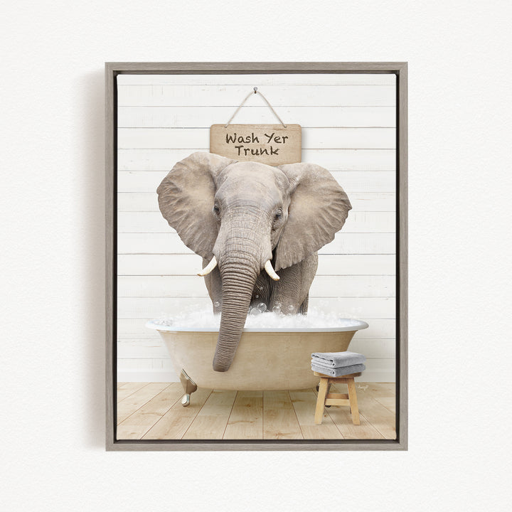 A gray elephant standing in a bathtub filled with water, with a sign above it that says "Wash Yer Trunk".