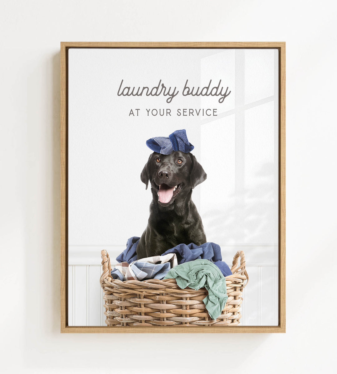 A black dog wearing a blue hat sits in a wicker basket filled with clothes, with the text "laundry buddy at your service" displayed above the image.