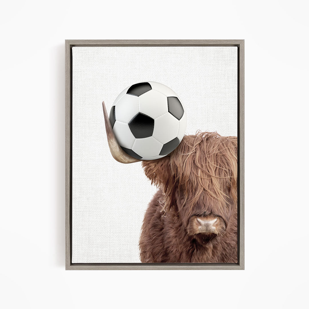A brown cow with long hair is balancing a soccer ball on its head.