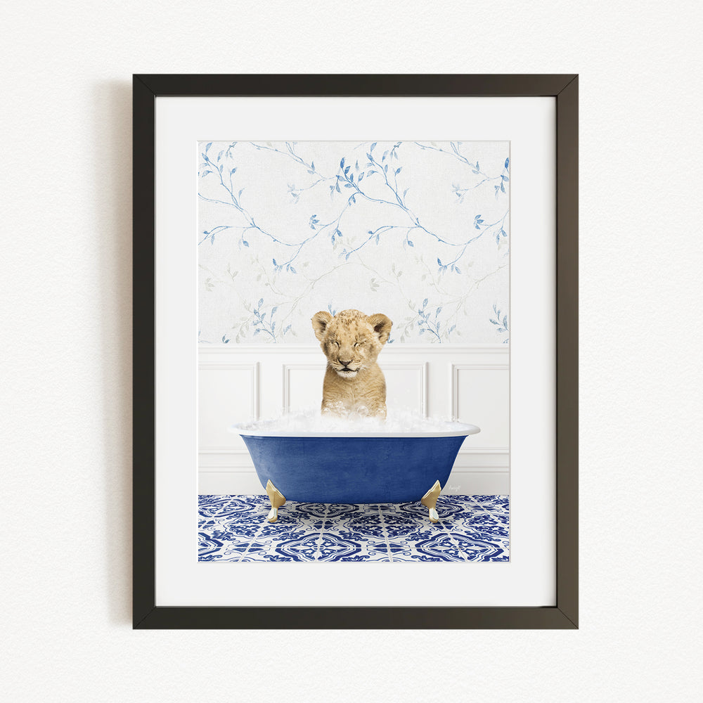 A young lion cub sitting in a blue bathtub filled with water, surrounded by a blue and white patterned rug.
