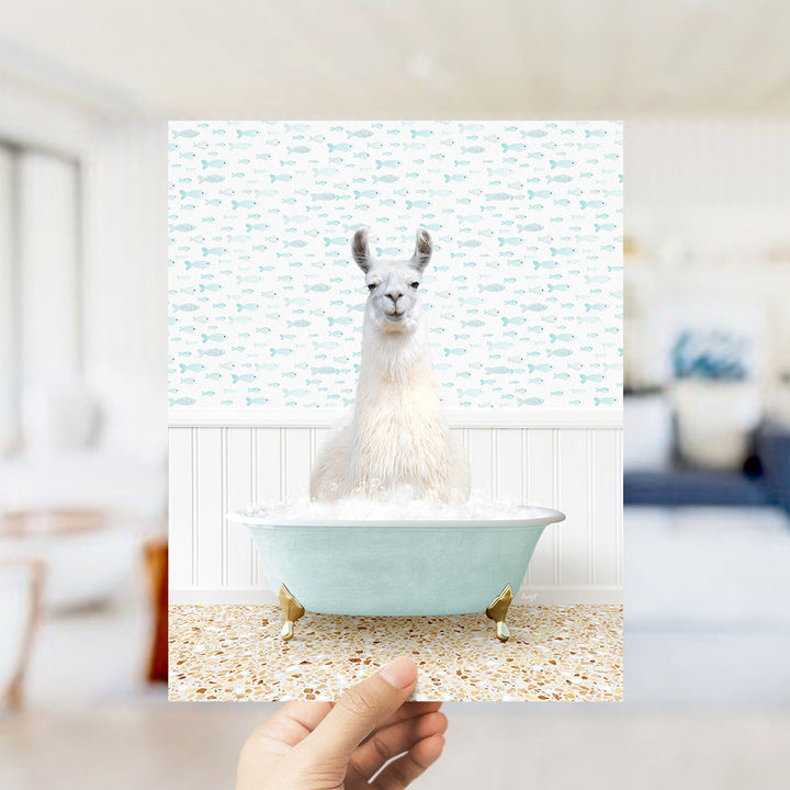 A white llama sitting in a light blue bathtub filled with bubbles, surrounded by a pattern of small fish.