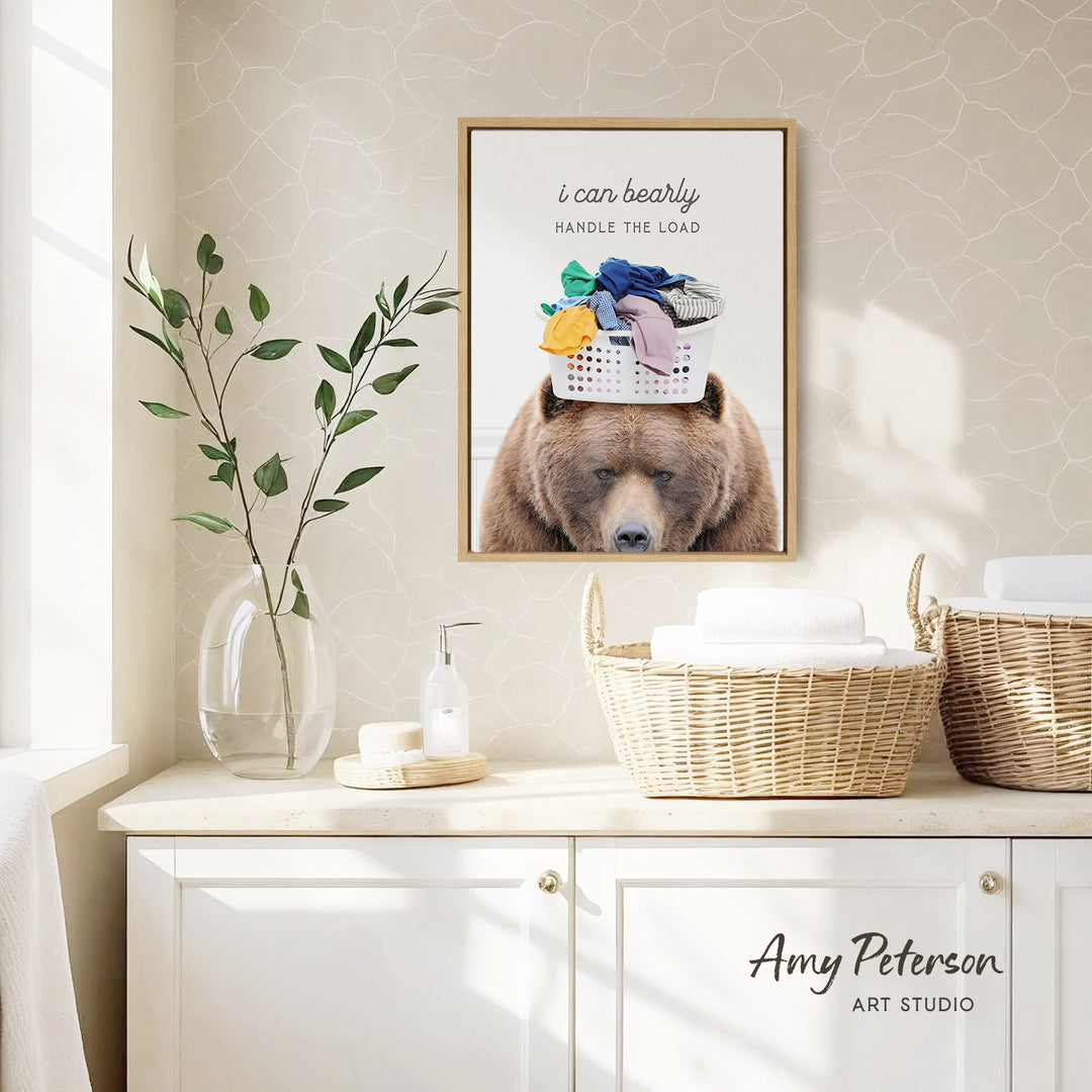 a framed poster of a bear with a laundry basket on its head, placed on a wall above a white cabinet.
