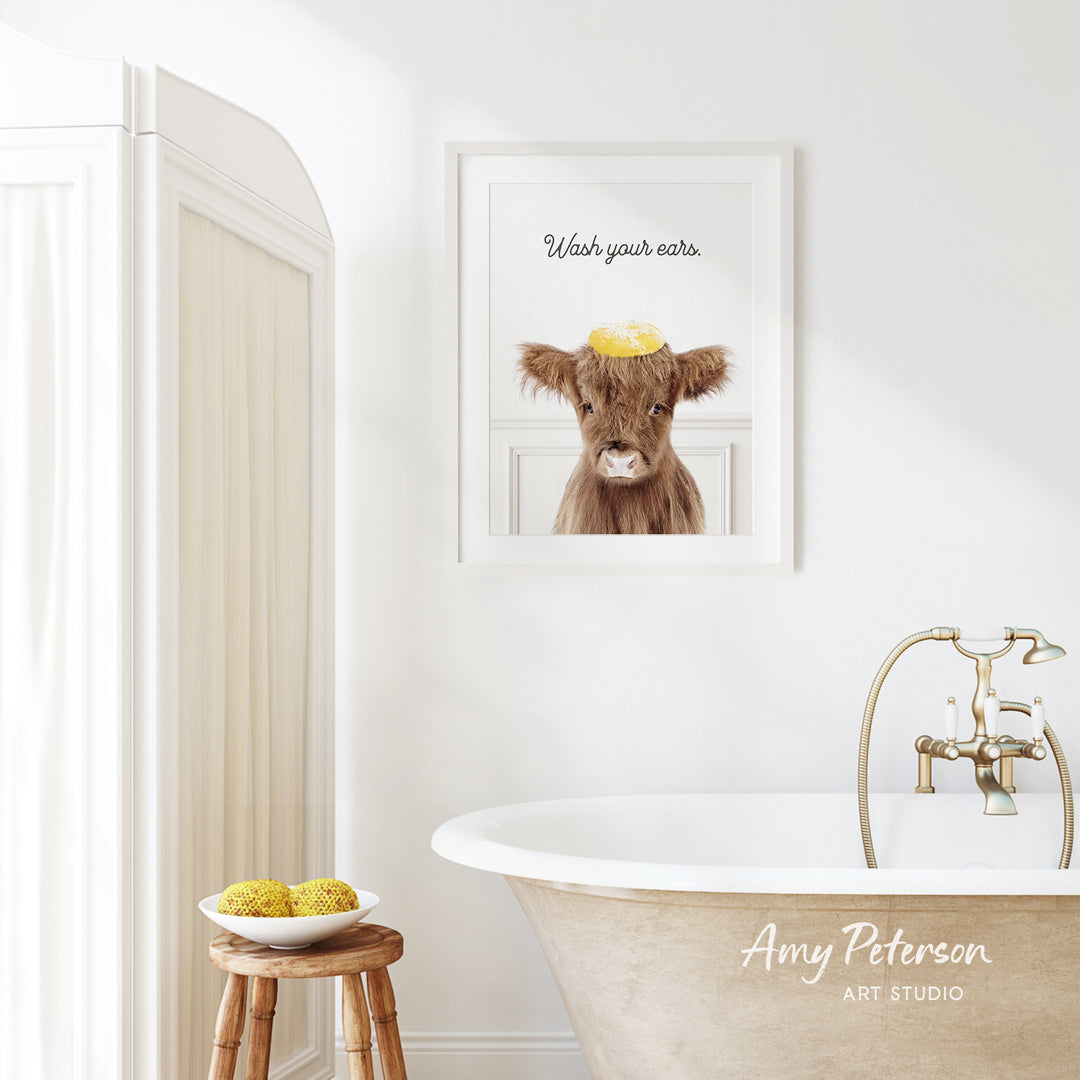 a bathroom with a framed picture of a cow on the wall, a wooden stool, a bowl of fruit, and a bathtub with a faucet.