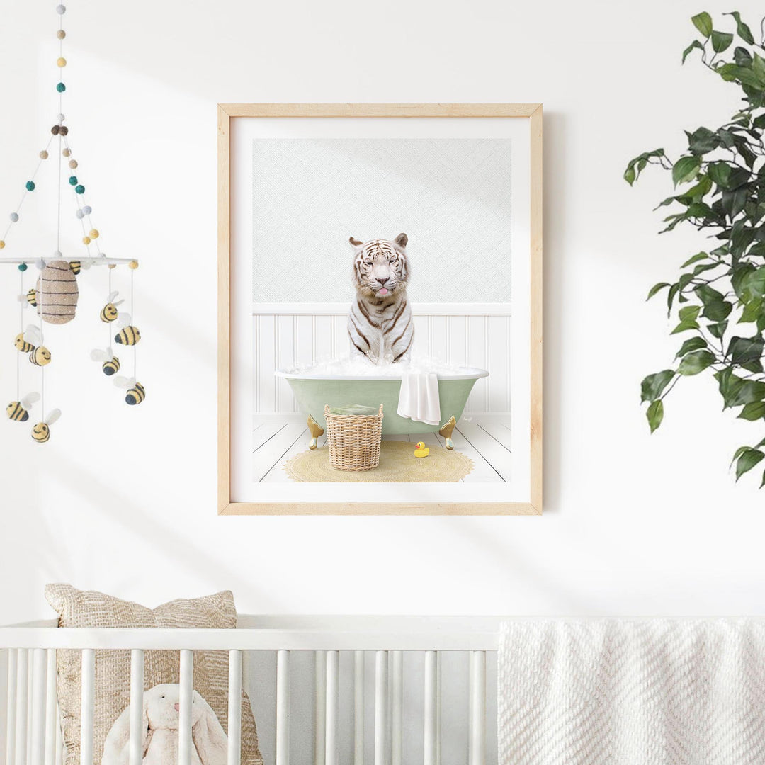 A framed image of a tiger sitting in a bathtub, surrounded by a basket of toys and a potted plant, is displayed on a white wall in a nursery setting.