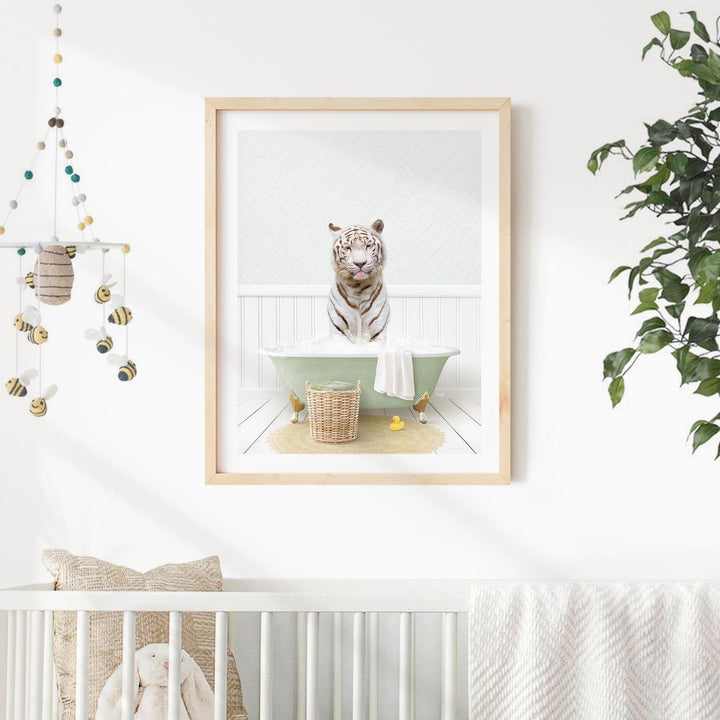 A framed image of a tiger sitting in a bathtub, surrounded by a basket of toys and a potted plant, is displayed on a white wall in a nursery setting.