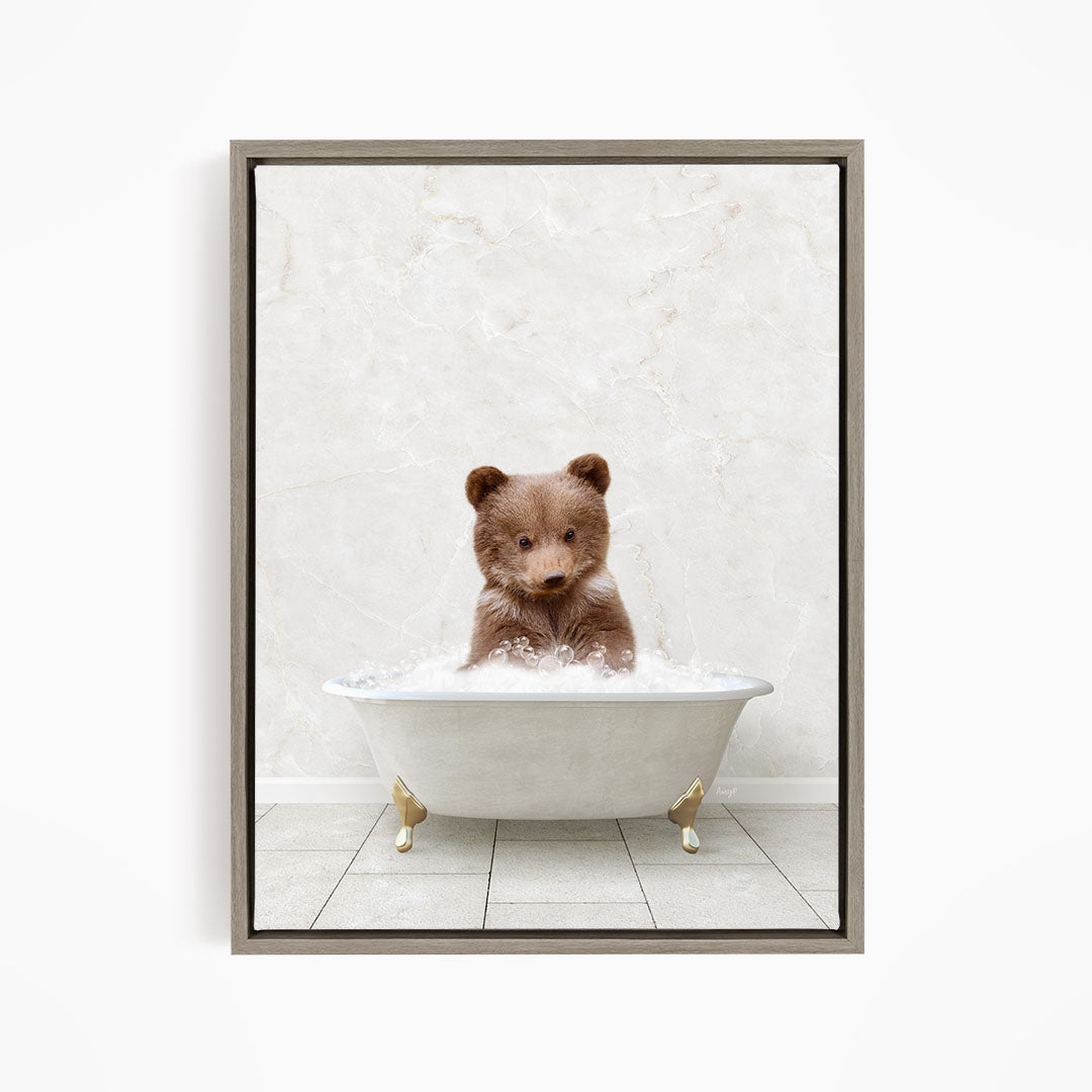 A cute brown bear sitting in a white bathtub filled with bubbles, looking directly at the camera.