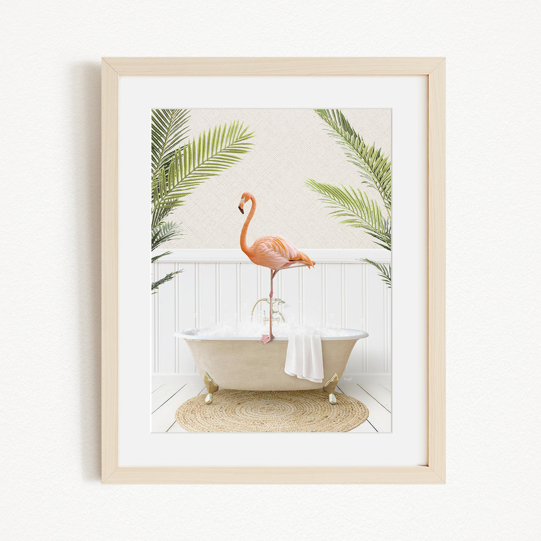 A framed image depicting a pink flamingo standing on a white bathtub, with a white towel and green palm leaves in the background.