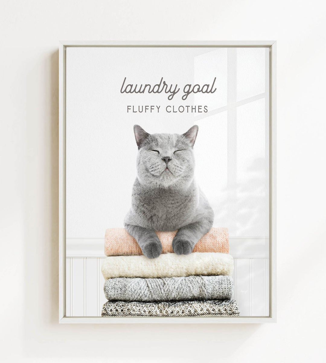 A gray cat sitting on a stack of clothes, with the text "laundry goal FLUFFY CLOTHES" above it.