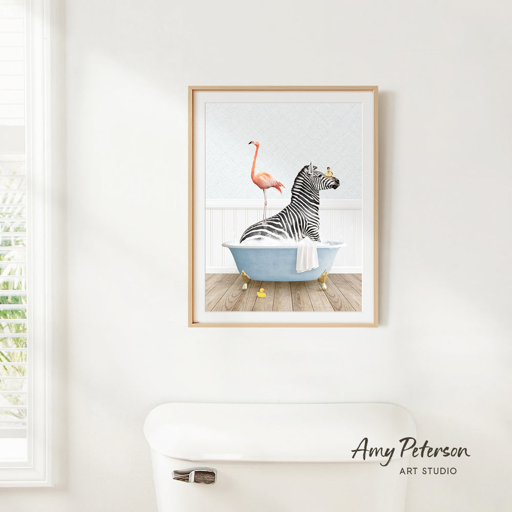 A framed illustration of a zebra sitting in a bathtub, with a pink flamingo standing on one leg next to it.