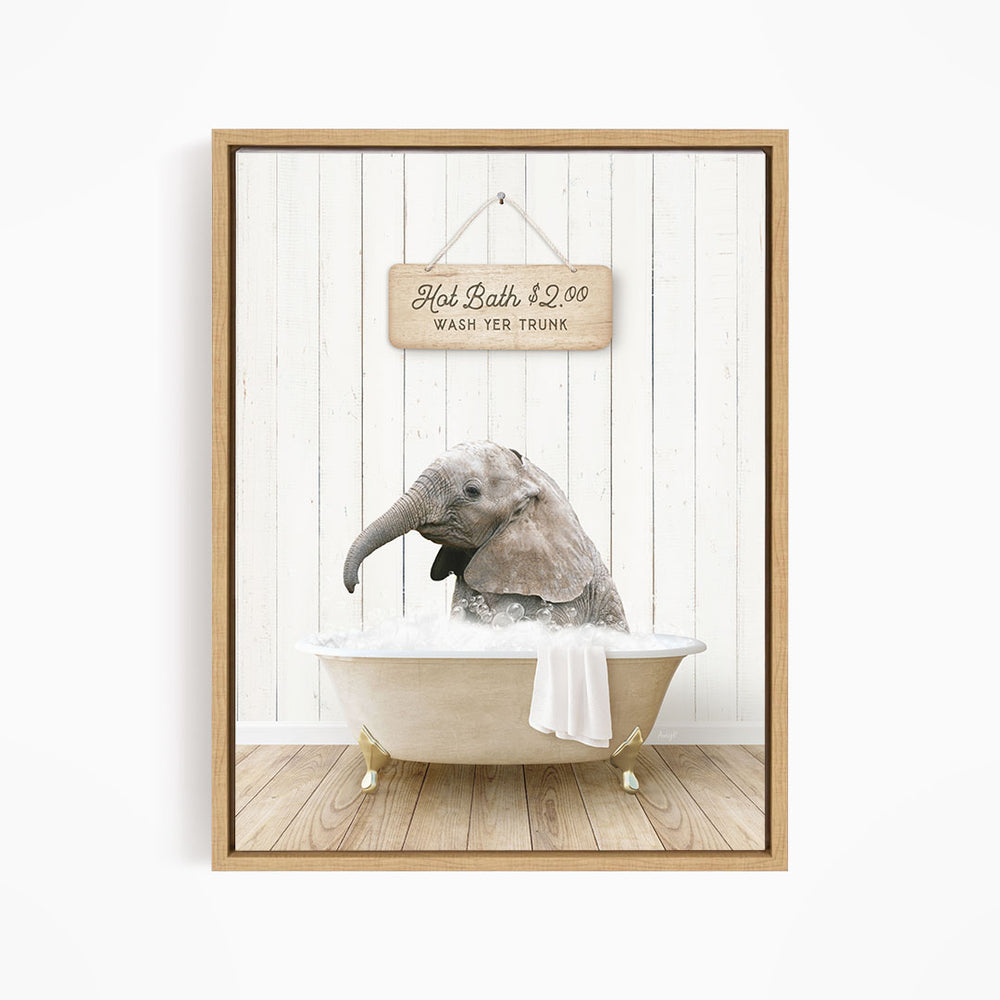 A wooden sign hangs above a bathtub with a gray elephant sitting in it, surrounded by a wooden floor and white walls.