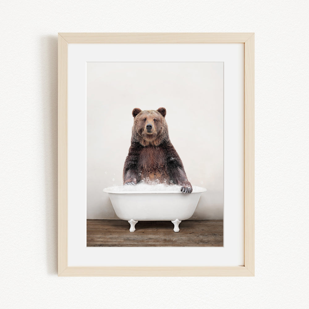 A brown bear sitting in a white bathtub filled with water, appearing to enjoy the bath.