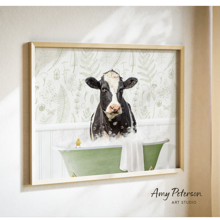 A framed image of a black and white cow sitting in a green bathtub filled with bubbles, with a yellow bird perched on the edge of the tub.