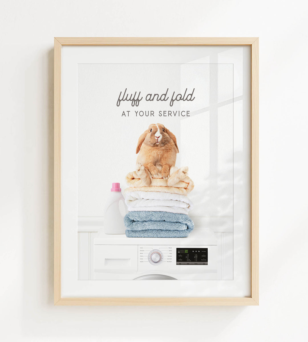 A framed image of a fluffy rabbit sitting atop a stack of folded towels, with the text "fluffy and folded at your service" written above it.