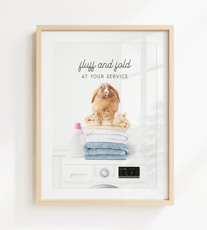 A framed image of a fluffy rabbit sitting atop a stack of folded towels, with the text "fluffy and folded at your service" written above it.