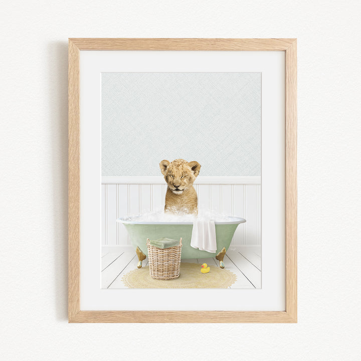 A young lion cub sitting in a green bathtub filled with water, surrounded by rubber ducks and a basket.