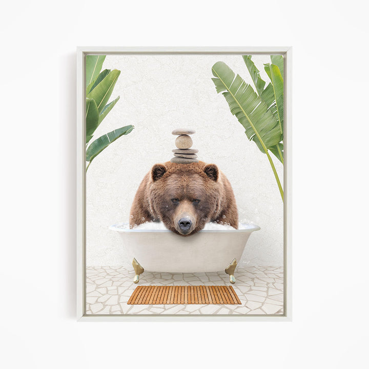 A brown bear is sitting in a white bathtub filled with water, surrounded by green leaves and a wooden mat on the floor.