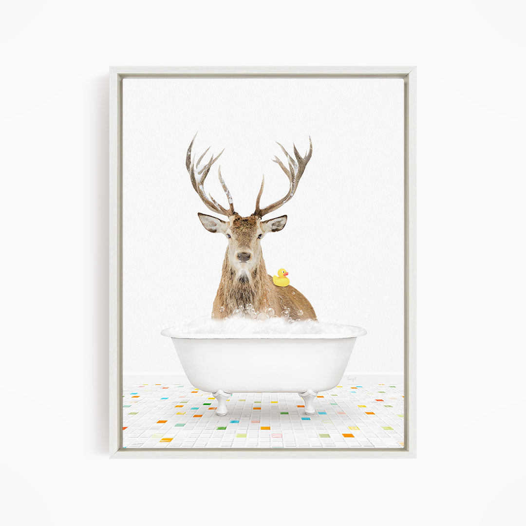 A deer with large antlers is sitting in a white bathtub filled with bubbles, with a yellow duck perched on its back.