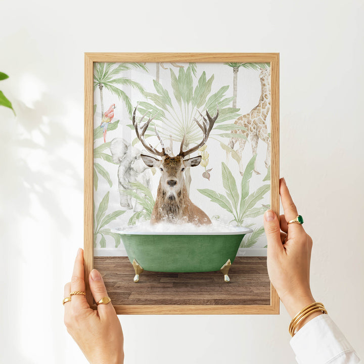 A person's hands are holding a framed picture of a deer in a bathtub, surrounded by tropical foliage.