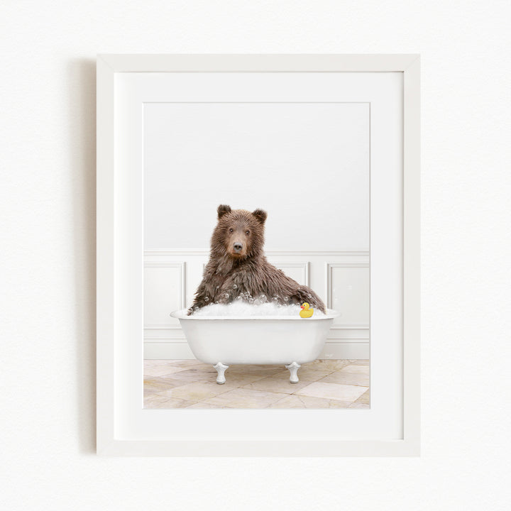 A brown bear sitting in a white bathtub filled with water and bubbles, with a yellow rubber duck floating in the water.