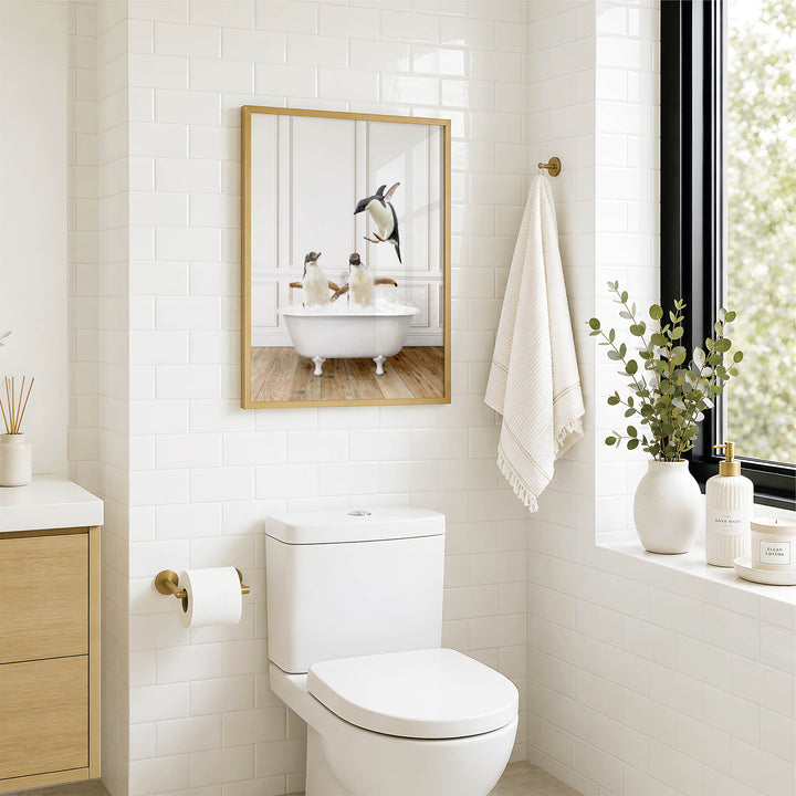 A modern bathroom with a white toilet, a framed image of penguins in a bathtub, and a window with greenery on the sill.