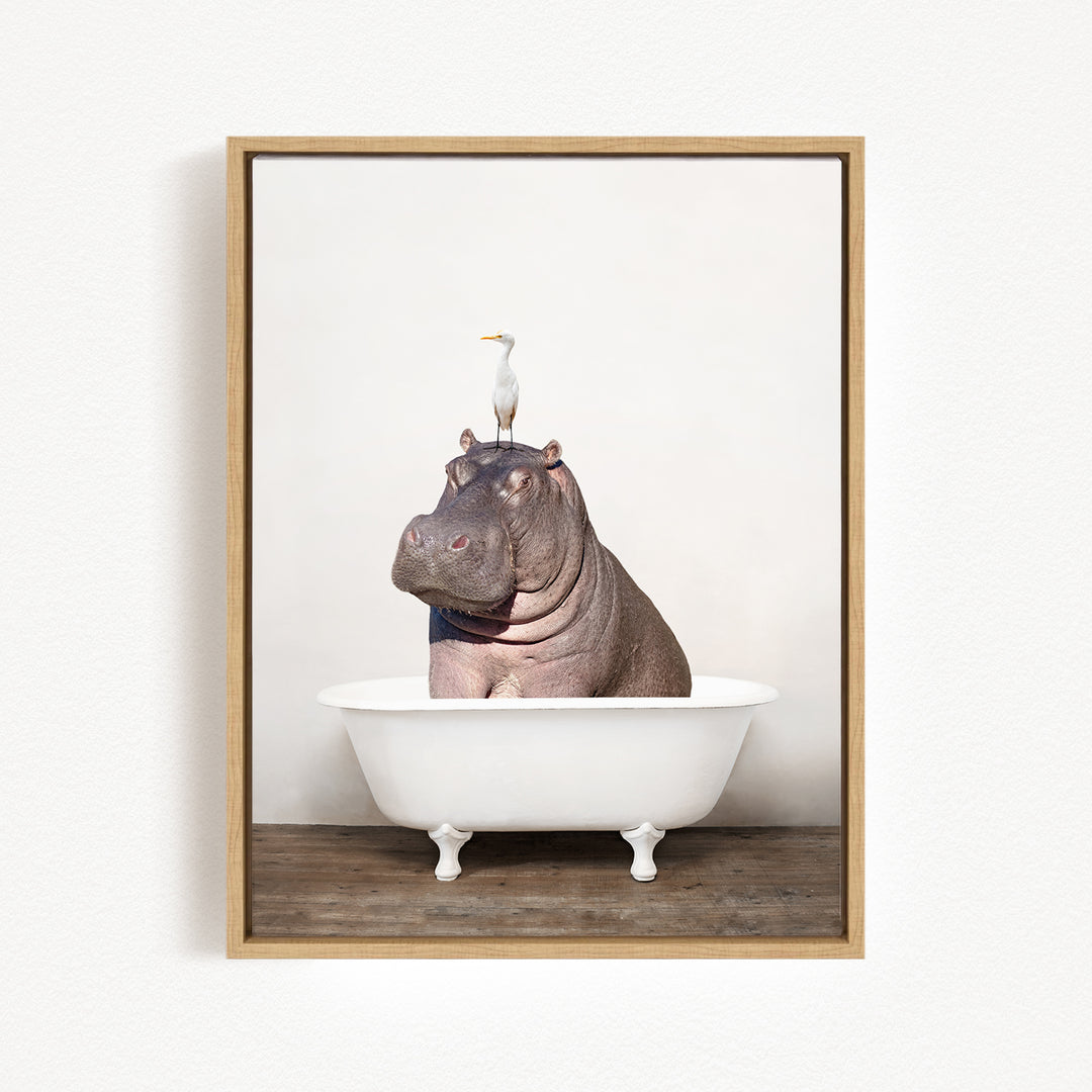 A framed image depicting a hippopotamus sitting in a bathtub, with a bird perched on its head.